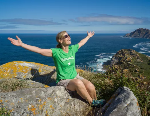 Guest on sunny hilltop, arms outstretched, ocean behind them.