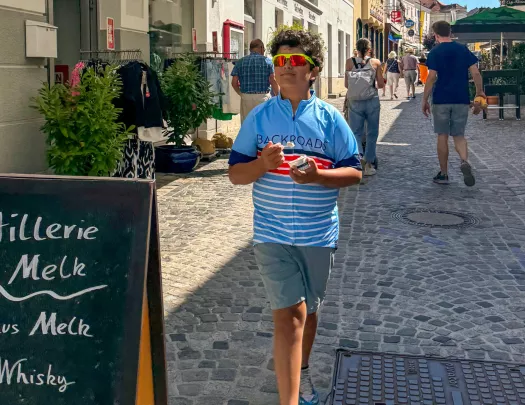 Boy wearing sunglasses, walking on a stone pathway in a town center