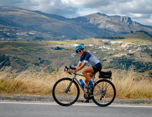 Woman smiling while biking on an asphalt road, with a large valley in the background