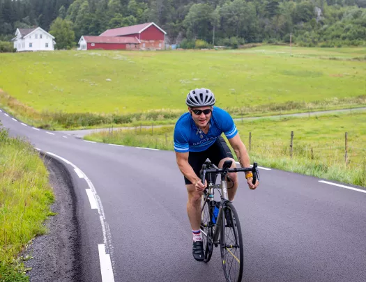 Man riding bike on asphalt road through a grassy field