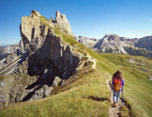 Woman hiking on a dirt trail towards the edge of a cliff