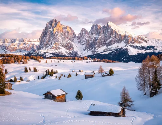 A snowed in plain with small houses and mountains in the background