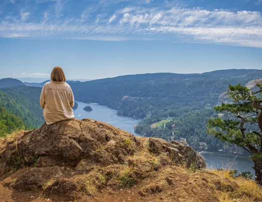 Woman sitting on a large boulder on top of a hill, looking down at the water