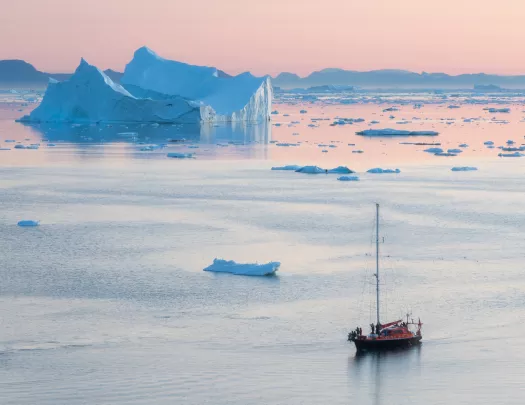 a ship floating on reflective water during a pink sunset