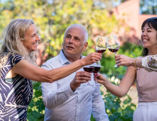 Two women and one man holding up wine glasses and smiling
