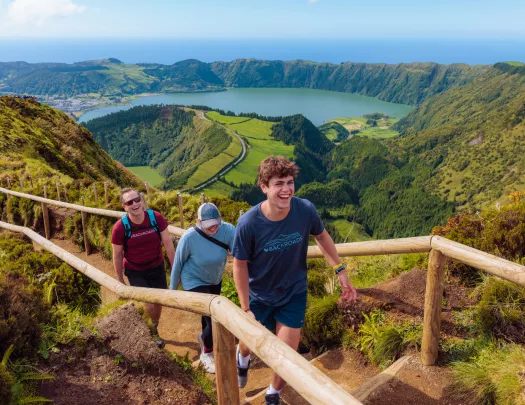 Three people walking on a dirt path that is on top of a hill, with a large valley in the background