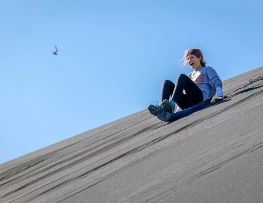 Girl on a plastic sled sliding down a hill of sand