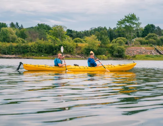 Two men inside of a yellow kayak, paddling in an open lake