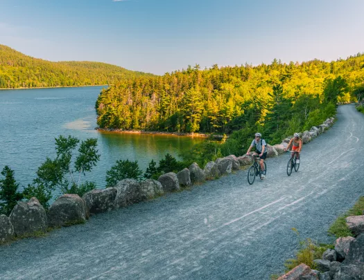 Man and woman riding their bikes on a gravel road next to a lake