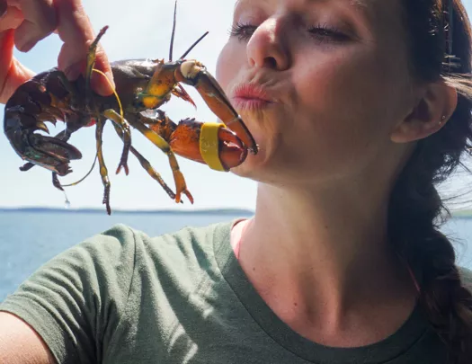 Woman holding up a baby lobster wile puckering her lips