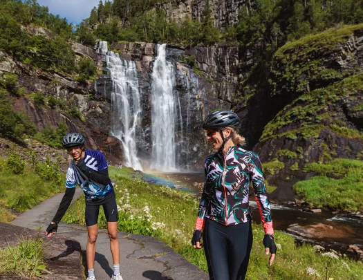 Two guests in cycling kits with a waterfall