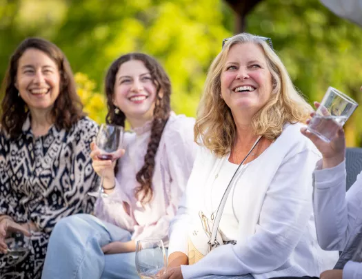 Three women smiling while looking up, holding up glasses of wine