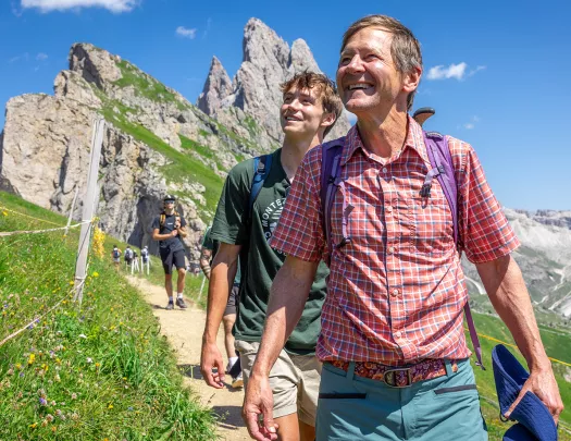 Two men smiling while looking up to the sky, while walking on a dirt trail