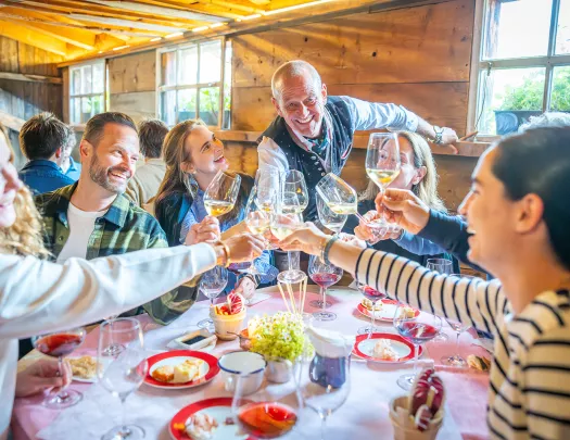 Group of people around a circular table, raising their wine glasses for a toast while smiling