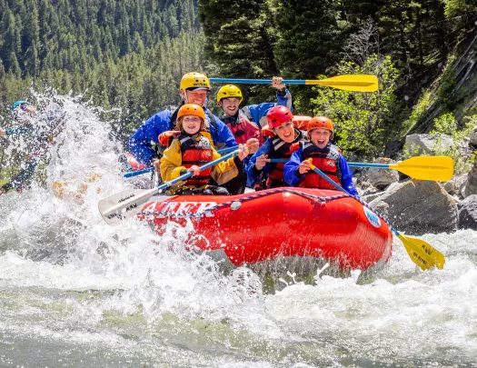 Group of adults and kids on a red raft in the middle of a river