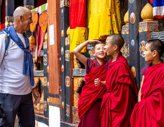 Man smiling and looking at 3 monk children in robes