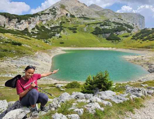 Woman sitting down and smiling, pointing at a small lake