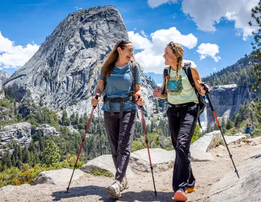two women with hiking poles hike in yosemite