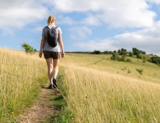 Woman walking through a field of tall weeds in a valley