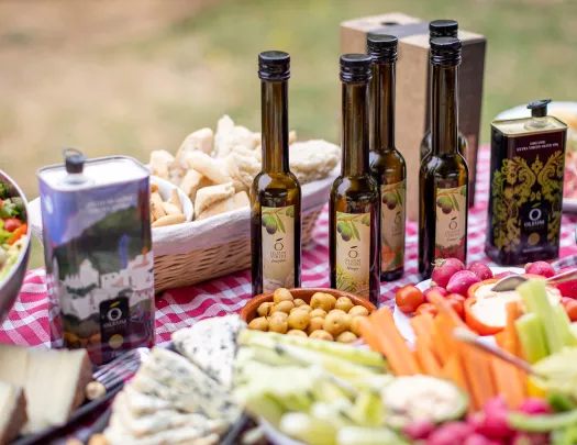 Table full of vegetables and snacks, and 5 bottles of olive oil
