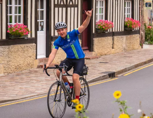 Man smiling while riding a bike on a road with one arm up