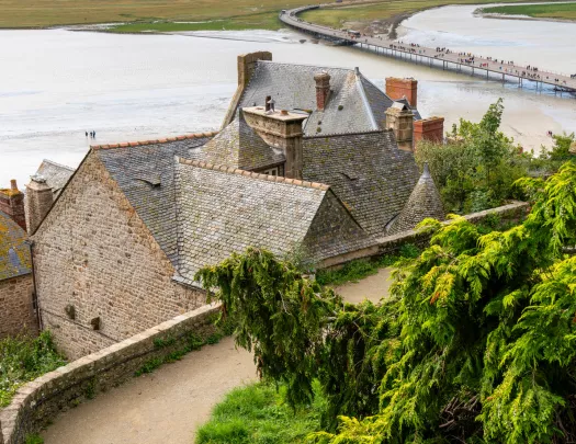 Top view of a stone building, with a dirt road and a large lake in the background