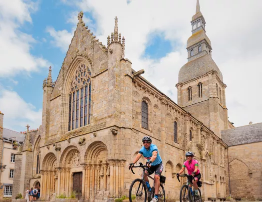 Man and woman biking in front of a stone cathedral