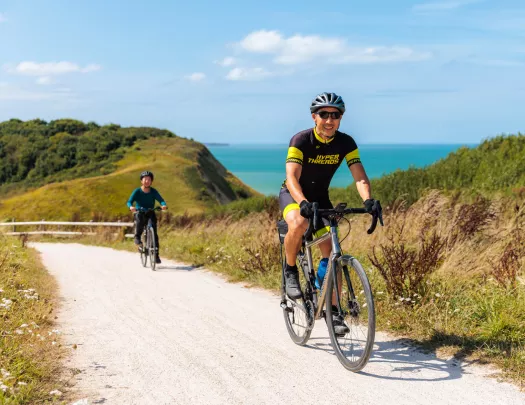 Man and woman biking on a sandy trail with the ocean in the background
