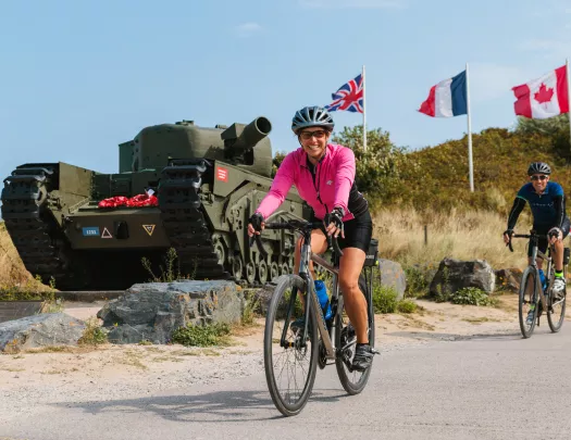 Woman in pink, biking in front of a green tank with flags waiving in the background
