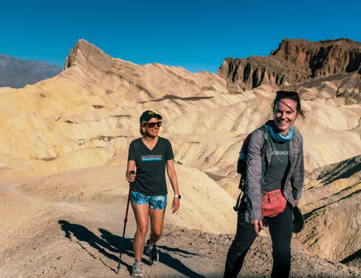 Two women ascending a rocky trail with large canyons in the background