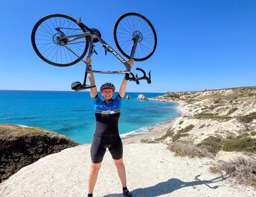 Person smiling while carrying a bike over their head, with the ocean in the background