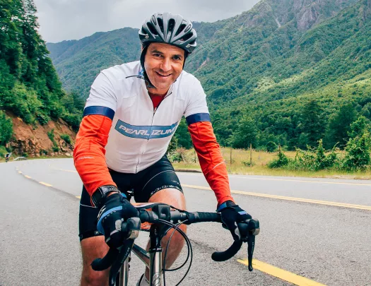 Man wearing biking gear and riding a bike on a road, with mountains in the background