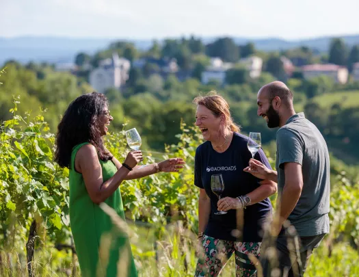 Two women and one man standing in a vineyard while holding glasses of wine