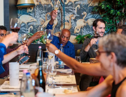 Group of people laughing and raising glasses of wine around a dining table