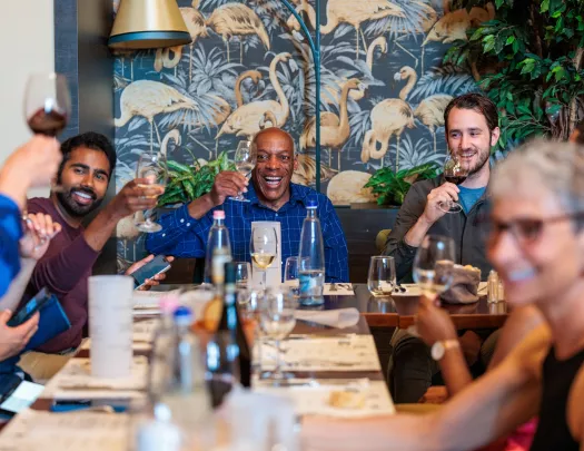 Group of people smiling at a dining table, raising their glasses of wine