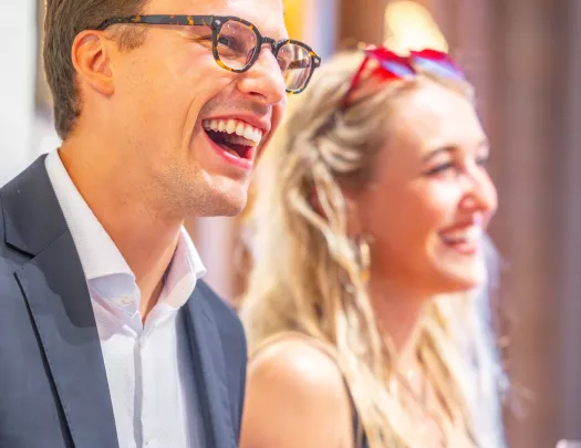Man wearing a suit and a woman in the back smiling