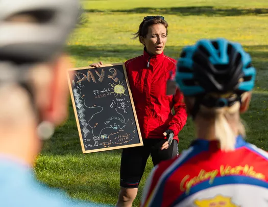 Woman holding up a chalkboard while talking to a group of bikers