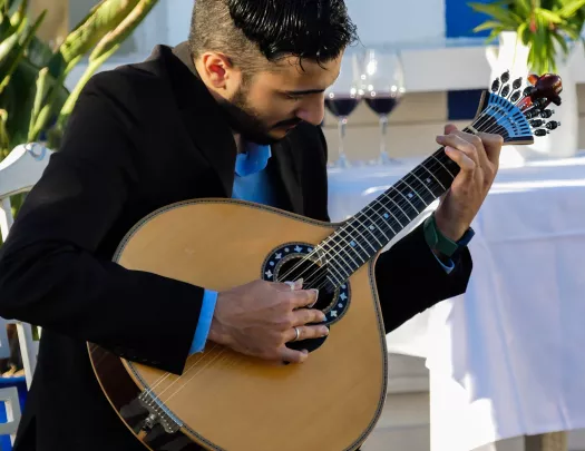 Man playing a guitar with a white table with wine glasses in the background