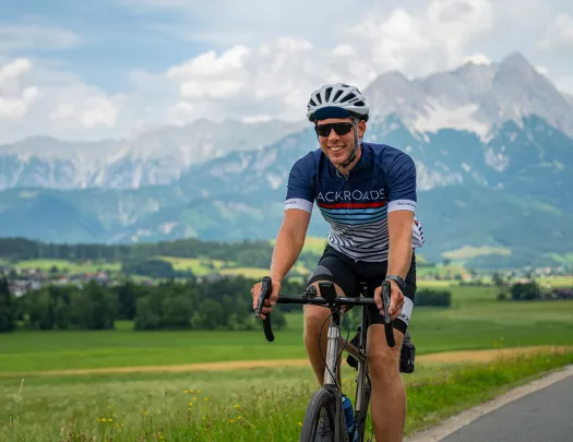 Man riding a bike on an empty road, with a large field and tall mountains in the background