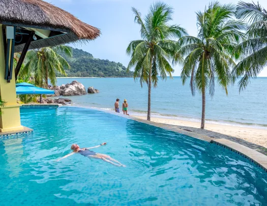 Woman floating in a pool, with views of the beach nearby