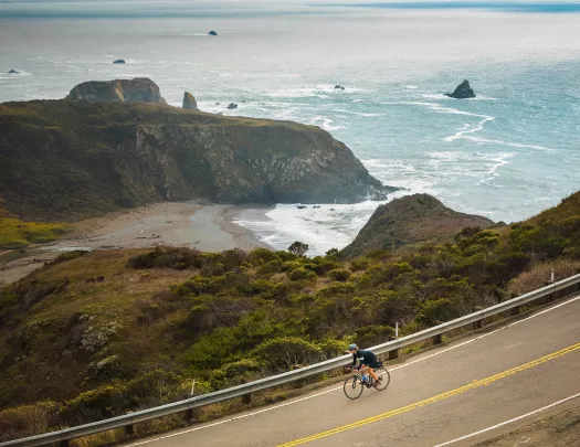 Person riding a bike on an empty road, with views of the ocean in  the distance