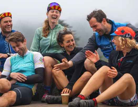 Group of people wearing biking gear, laughing while sitting on a ledge