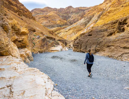 Woman walking a rocky trail in between two orange canyons