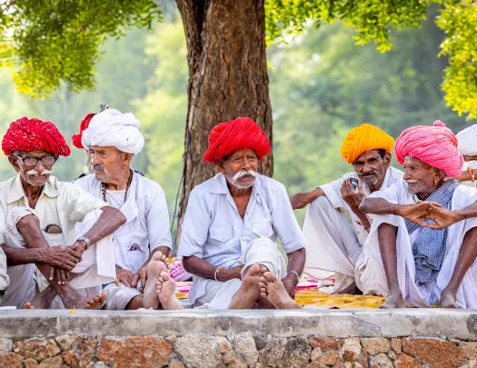 Group of Indian men wearing traditional headwear, sitting on a stone barricade