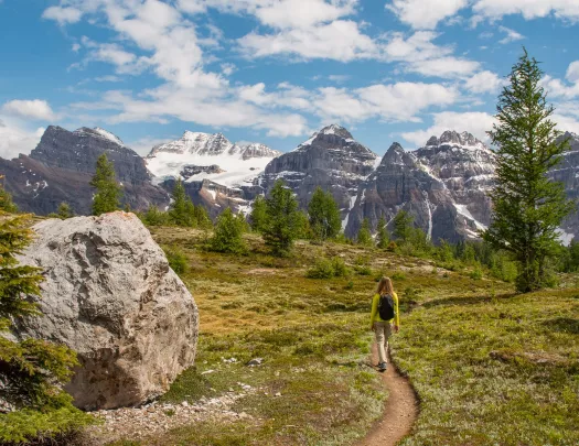 Woman walking along a dirt trail with large mountains in the distance