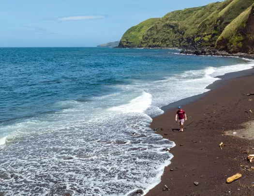 Man walking on a beach, with grassy mountains in the background
