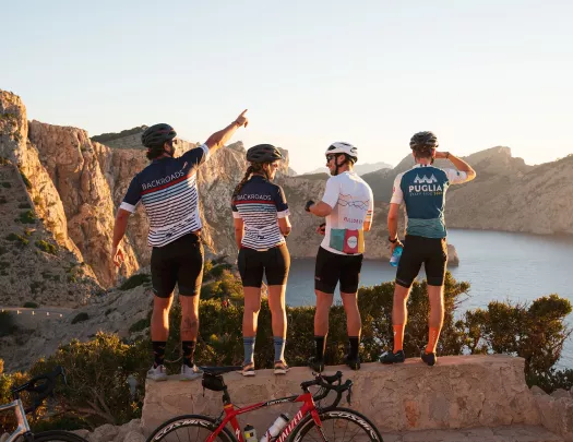 Group of people wearing biking gear, standing on a ledge looking out to a lake