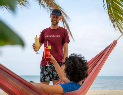 Man standing while raising a glass, with a person sitting on a hammock also raising their glass