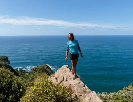 Woman standing on a boulder with the ocean in the distance