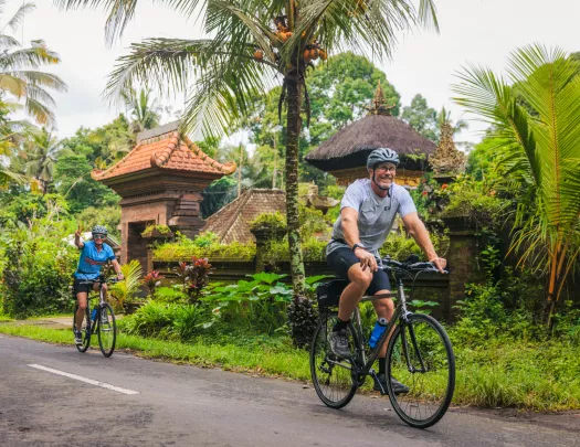 Man and woman biking on a road with jungle in the background